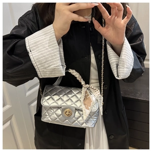 Detail of silver quilted handbag with golden twist lock and decorative silk scarf
