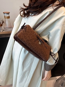 Brown leopard print bow shoulder bag with heart charm shown on model in warm indoor setting