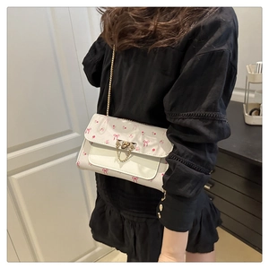 Modèle portant un sac bandoulière blanc à fleurs cerises avec chaîne dorée