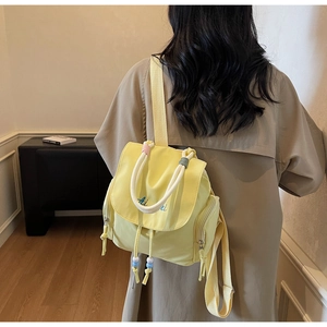 Detail des gelben Nylon-Rucksacks mit weißen Seilgriffen und bunten Perlenverzierung