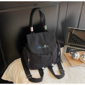 Detail eines schwarzen Nylonrucksacks mit Stickerei und Seitentaschen auf einem Bett