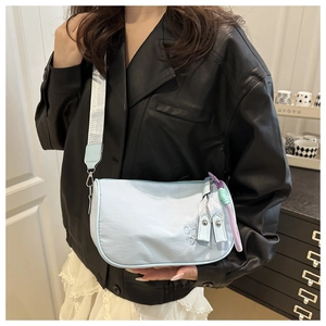 Detail of light blue nylon shoulder bag featuring wide strap and colorful zipper charms
