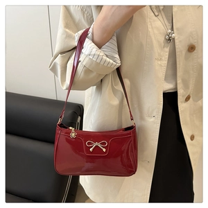 Detail of red patent leather handbag with gold bow buckle and floral charm on model