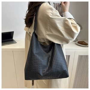 Side view of a black woven tote bag shown on a model in a cozy, bright office setting