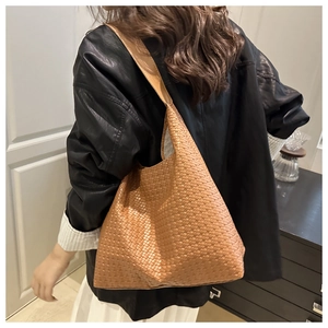 Caramel brown woven tote bag worn by a model in a minimalist indoor setting