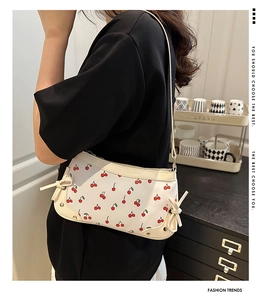 Detail of cream shoulder bag with cherry print and yellow bows worn by model