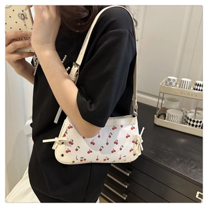 Detailed view of the side bow tie decoration on a white cherry print shoulder bag