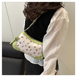 Close-up of cherry print on white leather underarm bag with green trim and metal rivets