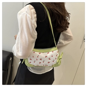 Detail view of the cherry print shoulder bag featuring side bow and green strap accents