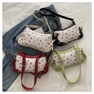 Detail of four colorful cherry print shoulder bags displayed on denim and white fabric