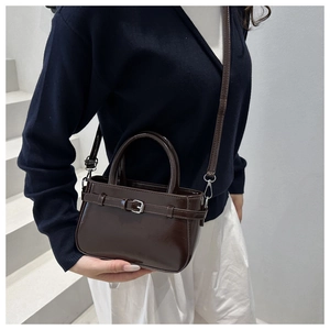Detail of a dark brown glossy leather handbag with silver buckle and crossbody strap