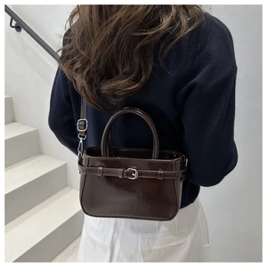 Detail view of glossy dark brown patent leather handbag with silver buckle and top handles