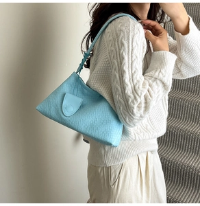 Detail of light blue woven bucket bag with magnetic flap worn by a model in a minimal setting