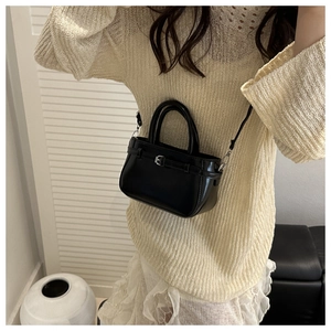 Detail view of a black mini crossbody bag with a silver metal buckle worn by a model