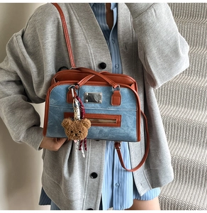Détail du sac cabas en denim bleu avec garniture en cuir brun et breloque ours peluche