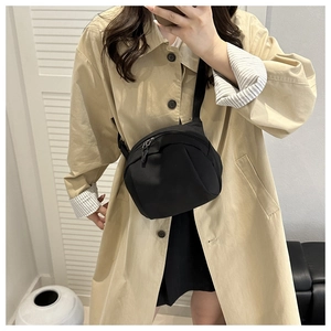 Minimalist black crescent crossbody bag worn with a stylish trench coat in a modern setting
