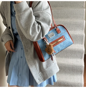Detail der blauen Denim-Einkaufstasche mit braunem Lederbesatz und süßem Bär-Anhänger