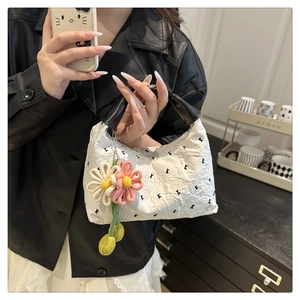 Close-up of cream crossbody bag featuring pleated texture and woven flower pendant