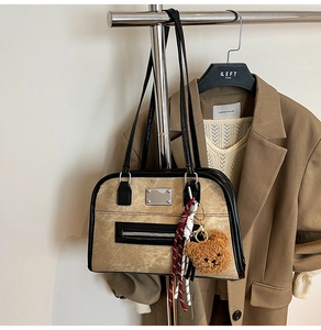 Retro khaki Boston bag with black trim and bear charm shown on a stylish autumn outfit