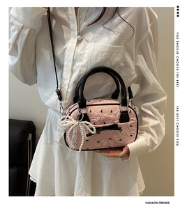 Détail d'un sac Boston rose avec imprimés nœuds noirs et pendentif en dentelle et perles
