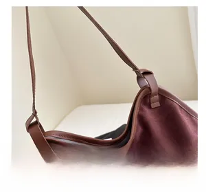 Detail of burgundy faux suede bucket bag with brown leather trim and reinforced stitching