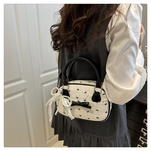Detail of white ruffled handbag featuring black bow patterns and elegant lace pearl charm