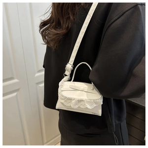 Detailed side view of white lace bow crossbody bag worn by model over dark clothing