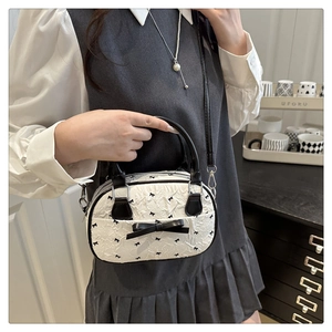 Detail of white pleated mini bag featuring black bow patterns and dual top handles