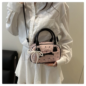 Detail of pink embossed crossbody bag with black bow and elegant pearl lace charm