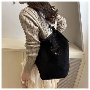 Detail of a black faux suede tote bag with a cylindrical leather tassel charm on a model