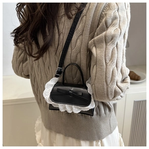 Detailansicht einer schwarzen Mini-Umhängetasche mit Spitze und Schleife am Modell
