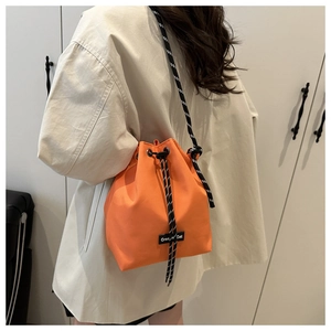 Detail view of bright orange drawstring bucket bag with black and white woven rope strap