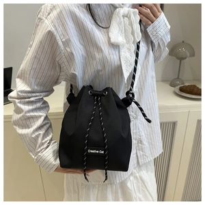 Close-up of a black nylon drawstring bucket bag with a Creative Cat woven strap detail