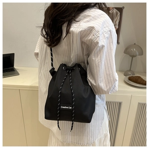 Detail of a black bucket bag showing the Creative Cat label and woven drawstring closure