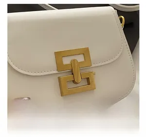 Close-up of stylish white leather saddle bag featuring a bold gold geometric lock design
