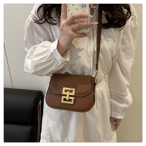 Detail view of a vintage brown crossbody bag with a gold geometric clasp on a white dress