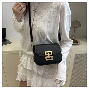 Detail of black square crossbody bag with gold geometric clasp on a white lace outfit