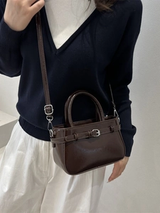 Deep brown glossy mini crossbody bag with decorative buckle and silver hardware on a model