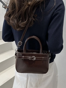 Dark brown glossy crossbody bag with decorative buckle shown on model in indoor setting