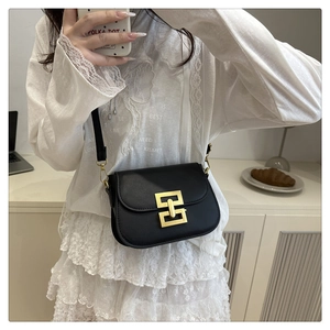 Detail of a black saddle crossbody bag with a gold buckle shown in a mirror selfie