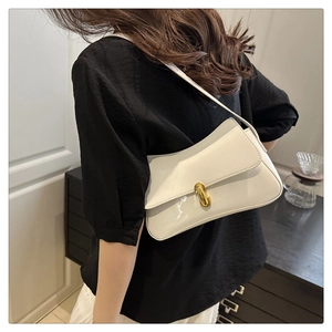 Model wearing a white patent leather shoulder bag with a cylindrical gold clasp