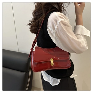 Detail of red patent leather shoulder bag with gold metal clasp worn by a model
