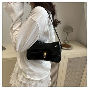 Glossy black patent leather underarm bag with gold clasp shown on model shoulder