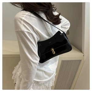 Detail of glossy black patent leather baguette bag with a golden metal press lock clasp