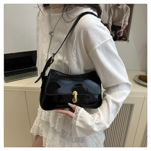 Detail of glossy black patent leather bag featuring a gold capsule-shaped twist lock buckle