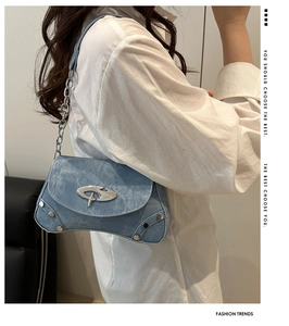 Detail of light blue denim shoulder bag with silver studs and futuristic metal logo