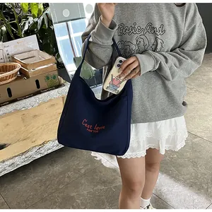 Détail du sac fourre-tout bleu marine en toile avec lettrage rouge porté par un mannequin