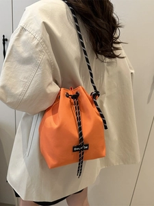 Vibrant orange drawstring bucket bag with stylish black and white rope shoulder strap