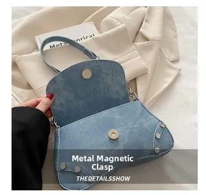 Detail of the blue denim baguette bag featuring a metal magnetic buckle and rivets