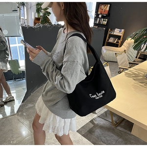 Close-up of black canvas tote bag with white C'est la vie artistic text and wide strap